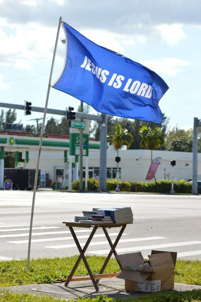 A street scene featuring a 'Jesus is Lord' flag and a table with books and boxes, emphasizing Christianity.